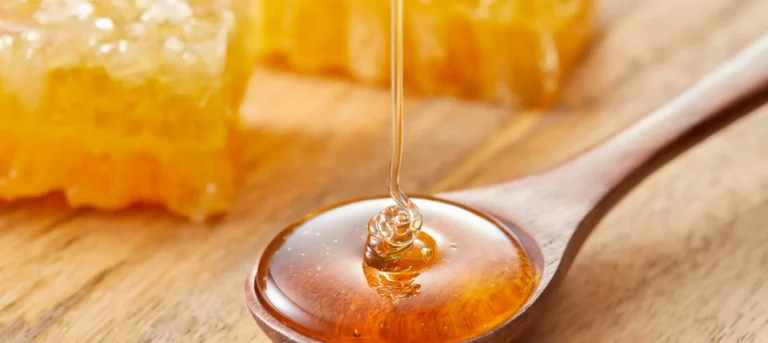 Liquid honey in a spoon with honeycomb in the background